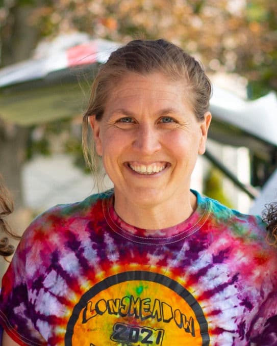 Elizabeth Morgan smiling outdoors in a tie-dye Longmeadow 2021 festival t-shirt