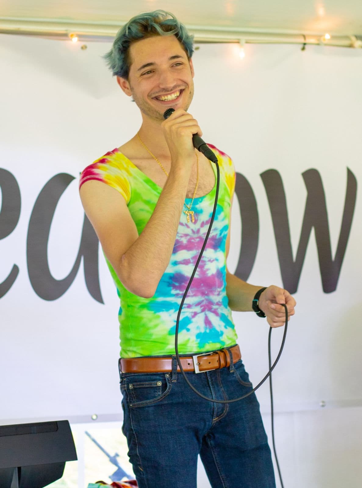 Nate Munic on stage with a microphone, wearing a tie-dye top, in front of a Longmeadow banner